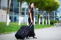 Vacation. Smiling female passenger proceeding to exit gate pulling suitcase through airport concourse Royalty Free Stock Photo