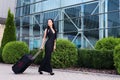 Vacation. Smiling female passenger proceeding to exit gate pulling suitcase through airport concourse Royalty Free Stock Photo