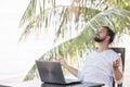 Vacation and technology. Work and travel. Young bearded man using laptop computer while sitting at beach cafe bar. Royalty Free Stock Photo