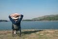 Asian woman wear hat and sitting relax on portable chair nearly lake at National Park.