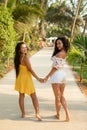 Vacation in tropics. Two lovely young Asian women, who turned around and smiled at camera, standing on path in hotel.