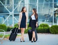 Vacation. Two happy girls traveling abroad together, carrying suitcase luggage in airport Royalty Free Stock Photo
