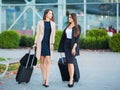 Vacation. Two happy girls traveling abroad together, carrying suitcase luggage in airport Royalty Free Stock Photo