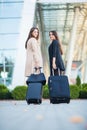 Vacation. Two happy girls traveling abroad together, carrying suitcase luggage in airport Royalty Free Stock Photo