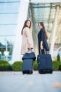 Vacation. Two happy girls traveling abroad together, carrying suitcase luggage in airport Royalty Free Stock Photo