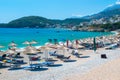 Vacationers on beautiful clean sand and pebble beach with umbrellas and sun loungers. Sunny mountains blue seaside landscape.