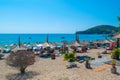 Vacationers on beautiful clean sand and pebble beach with umbrellas and sun loungers. Sunny mountains blue seaside landscape.