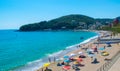 Vacationers on beautiful clean sand and pebble beach with umbrellas and sun loungers. Sunny mountains blue seaside landscape.