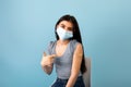 Vaccinated Indian teen girl in medical mask pointing at plaster bandage on her shoulder after getting covid-19 vaccine Royalty Free Stock Photo