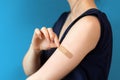 Vaccination against coronavirus. Woman in a blue t-shirt peels off a band-aid from her hand. Close-up. Dark blue Royalty Free Stock Photo