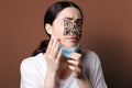 Vaccination. Portrait of a woman with a QR code instead of eyes and nose, examining her new face. Brown background. The