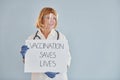 Vaccination saves lives banner. Senior female doctor in white coat is standing indoors