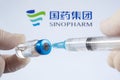 A vaccination syringe and a glass ampoule with a clear liquid on a blue background with the logo of Sinopharm pharmaceutical