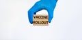 Vaccine rollout symbol. Hand in blue glove holds wooden blocks with words `vaccine rollout`. Beautiful white background. Copy