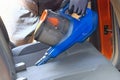 Vacuum cleaner in hands of driver. Cleaning of interior of automobile with blue vacuum cleaner, closeup. Car textile seats is