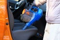 Vacuum cleaner in hands of driver. Cleaning of interior of automobile with blue vacuum cleaner, closeup. Car textile seats is