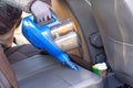 Vacuum cleaner in hands of driver. Cleaning of interior of the car with blue vacuum cleaner. Car textile seats is regular clean up