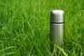 Vacuum insulated steel thermos bottle in the green grass at summer picnic
