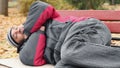 Vagabond in jacket and jeans sleeping on bench, trying to keep warm, poverty