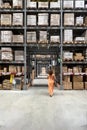 Woman in the warehouse of Ikea, a furniture store, passing under large shelves with packaged items ready for pick-up