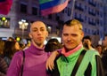 VALENCIA, SPAIN - Mar 08, 2020: Stylish Homosexual Couple in Gay Pride Parade Looking at Camera With Rainbow Flag Background