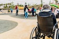 Valencia, Spain - May 1, 2019: Disabled elderly woman sitting back to back in a wheelchair while watching her grandchildren play Royalty Free Stock Photo
