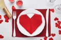 Valentinas day table setting white color with white silverware, red napkin folded as heart, candles, champagne, glasses on white