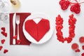 Valentinas day table setting white color with white silverware, red napkin folded as heart, candles, champagne, glasses on white