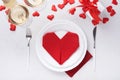 Valentinas day table setting white color with white silverware, red napkin folded as heart, candles, champagne, glasses on white b