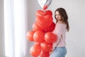 Beautiful woman on a grey background with a bunch of red balloons in the shape of a heart Royalty Free Stock Photo