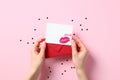 Valentine card mockup with lipstick kiss and red envelope in female hands over pastel pink background with confetti Royalty Free Stock Photo