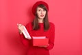 Valentine day concept. Sad woman opening empty box gift present. Elegant attractive model wearing red sweater and beret, looking Royalty Free Stock Photo