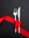 Valentine day dinner table setting. Fork and knife cutlery tied with red ribbon on black background, top view Royalty Free Stock Photo