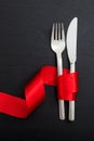 Valentine day dinner table setting. Fork and knife cutlery tied with red ribbon on black background, top view Royalty Free Stock Photo