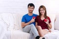 Valentine day relationships concept. Cheerful smile young couple sitting on white couch holding red heart in their hands Royalty Free Stock Photo