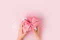 Valentine gift. Kids hands holding Gift box with pink bow on pastel pink background with glowing stars confetti. pastel colors. Royalty Free Stock Photo