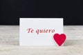 Valentine greeting card on wooden table with text written in spanish Te quiero, which means I love you