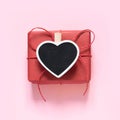 Valentine`s card. Red gift with clothespin as heart with space for text on chalkboard on pastel pink background. Top view.