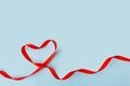 Valentine's Day background February 14th. Heart made of red satin ribbon on blue background.