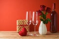 Valentine`s day background. Wooden table with glasses, wine bottle and rose flowers over red background Royalty Free Stock Photo