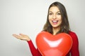 Valentine`s Day. Beautiful young woman wearing red dress and holding a red heart air balloon showing your product or text on whit Royalty Free Stock Photo