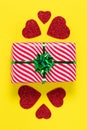 Valentines Day card. Wrapped gift. Minimalistic design. Festive present and red hearts on a yellow paper background, romantic