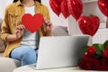 Valentine's day celebration in long distance relationship. Woman holding red paper heart while having video chat with her