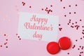 Valentine`s day composition with greeting card with text, two macarons and heart shaped confetti on pink background