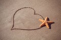 Valentine's day concept at beach. big orange starfish and drawn heart on sand texture.