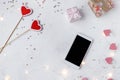 Valentine`s day concept. Hearts, confetti, smartphone, decor, lights on a light background