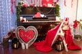 Valentine`s Day concept. Piano decorated with candles, red wooden hearts and flowers. Unfocused chair with red plaid