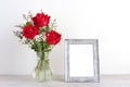 ValentineÃ¢â¬â¢s day concept, Red roses flower bouquet in glass vase and blank grey vintage wooden frame on table background with Royalty Free Stock Photo