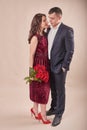 Valentine`s Day couple with roses on beige background. Portrait of happy young lovers with flowers. Picture showing man giving Royalty Free Stock Photo