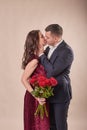 Valentine`s Day couple with roses on beige background. Portrait of happy young lovers with flowers. Picture showing man giving Royalty Free Stock Photo